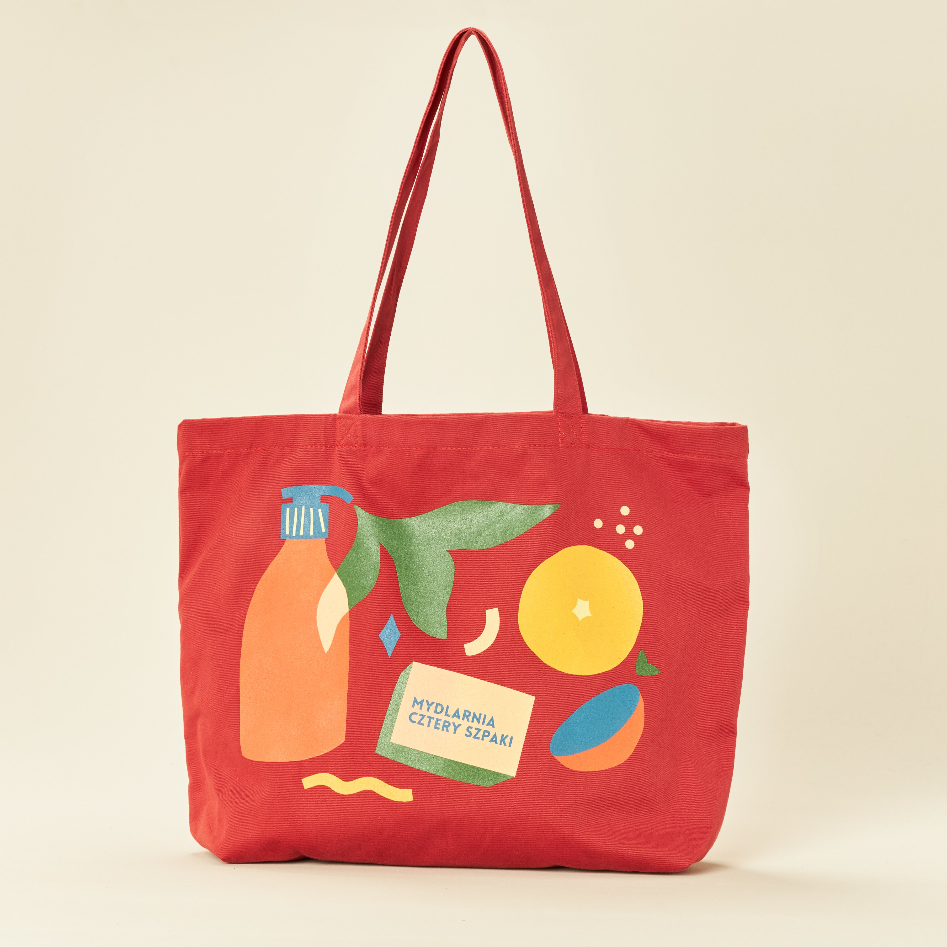 Czerwona torba z ilustracjami butelki, plasterków pomarańczy, zielonych liści i prostokąta z napisem MYDLARNIA CZTERY SZPAKI w kolorach niebieskim, żółtym, zielonym i pomarańczowym na jednolitym beżowym tle.