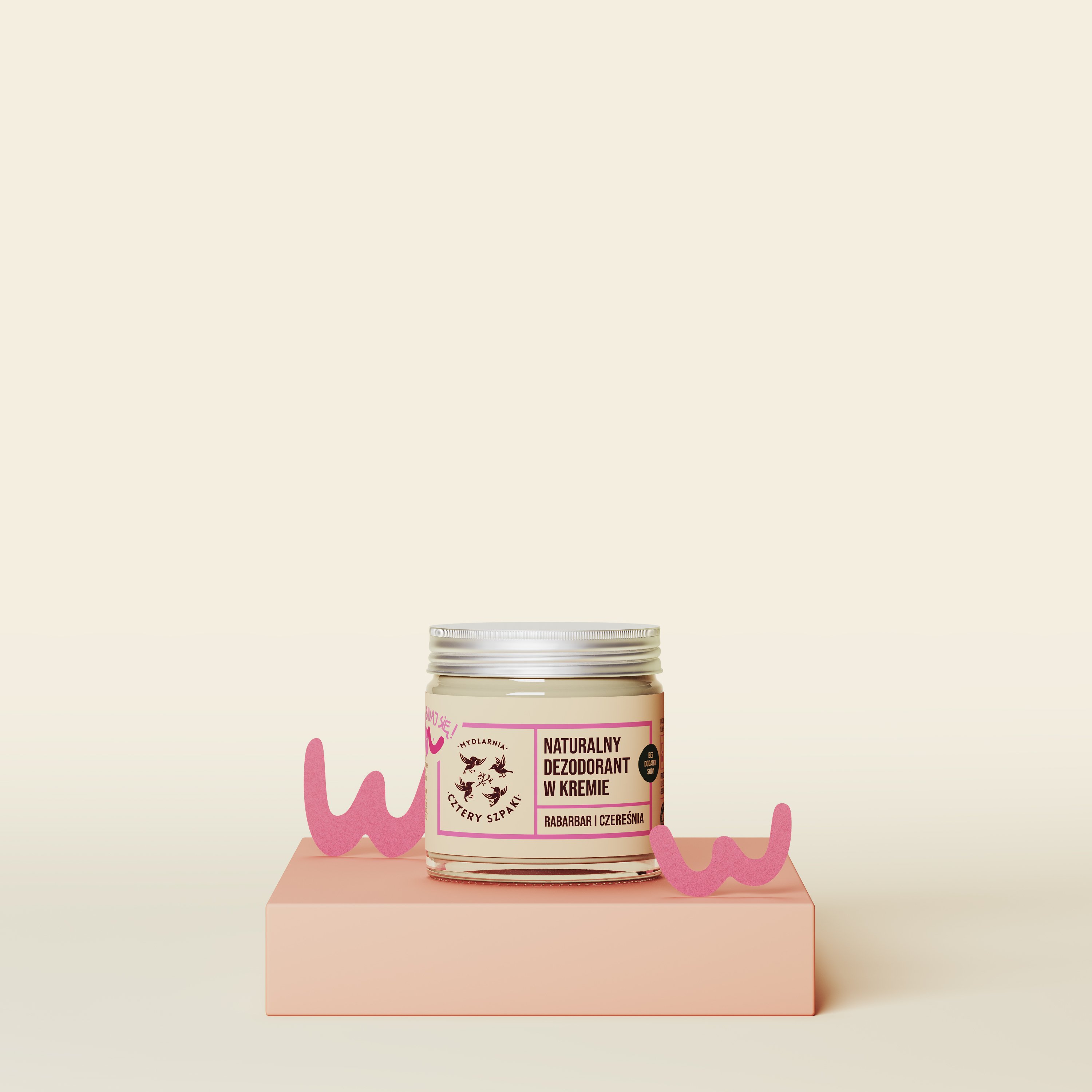 Słoiczek naturalnego dezodorantu w kremie z etykietą „Rabarbar i Czereśnia” wystawiony jest na platformie w kolorze brzoskwiniowym, z różowymi elementami dekoracyjnymi po obu stronach, na delikatnym beżowym tle.