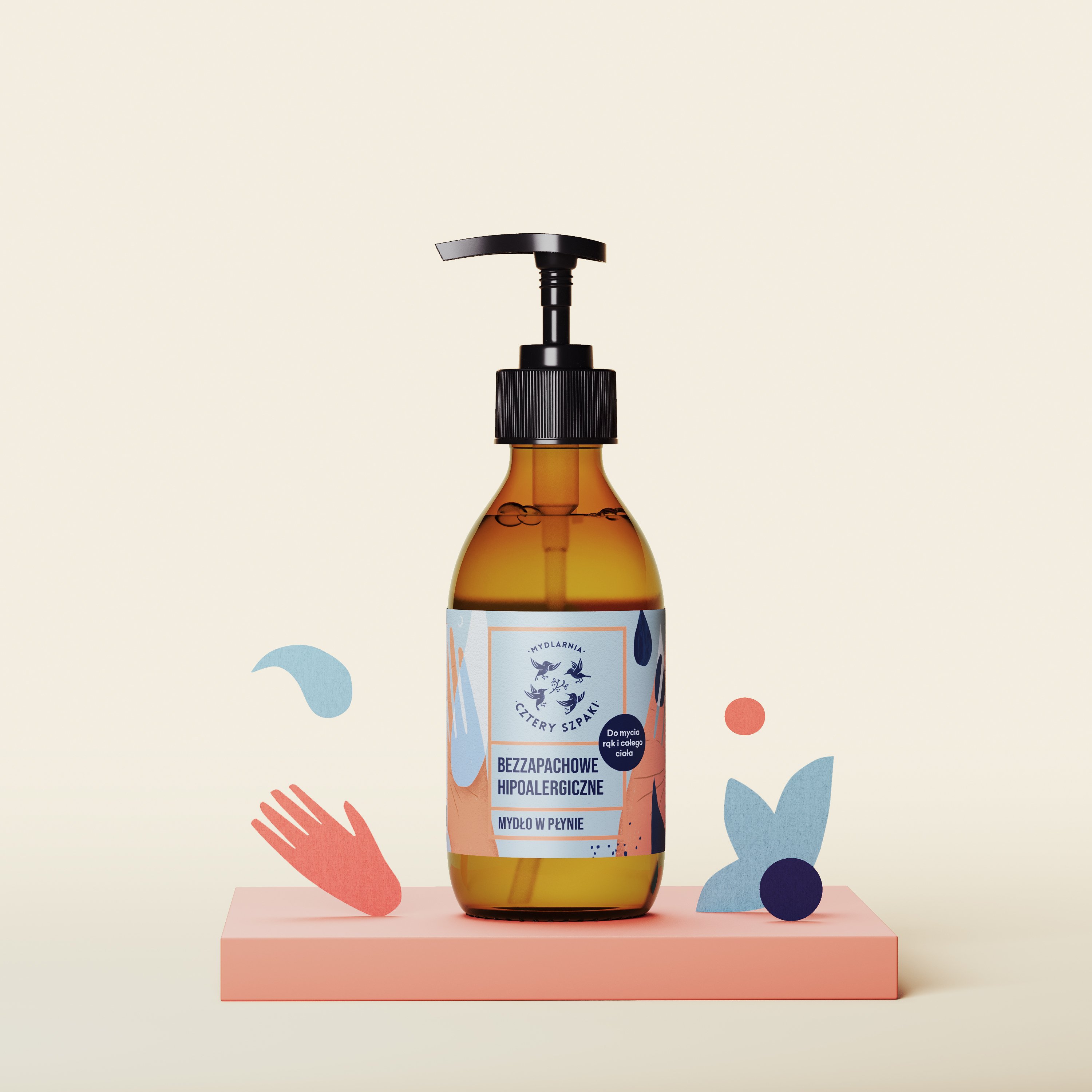 Na różowej platformie eksponowana jest brązowa butelka z pompką hipoalergicznego, bezzapachowego mydła w płynie. Etykieta zawiera niebieskie i pomarańczowe akcenty oraz zabawne abstrakcyjne kształty otaczające butelkę.