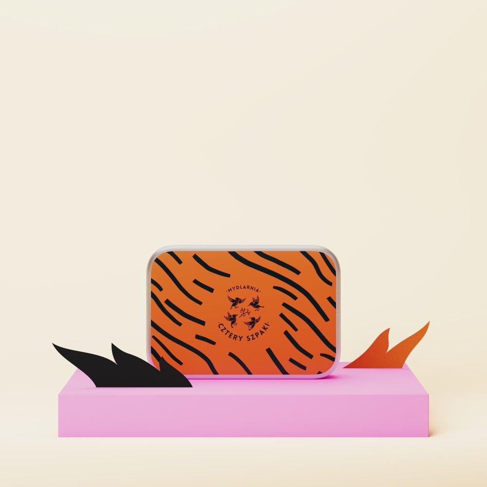 Prostokątna puszka z pomarańczowo-czarnym tygrysim paskiem stoi na różowej platformie, na której znajduje się napis „Mydlarnia Cztery Szpaki” i ilustracja ptaka pośrodku.