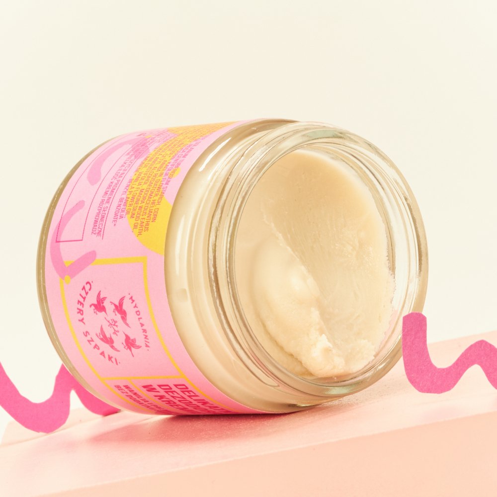 Zbliżenie na otwarty słoiczek produktu o kremowej konsystencji w kolorowym różowo-żółtym opakowaniu, idealny dla entuzjastów pielęgnacji skóry.