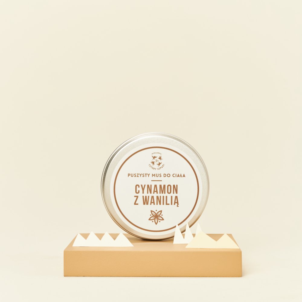 Puszka musu do ciała z etykietą „Cynamon z wanilią” jest eksponowana na beżowym stojaku z trójkątnymi akcentami, na pasującym neutralnym tle.