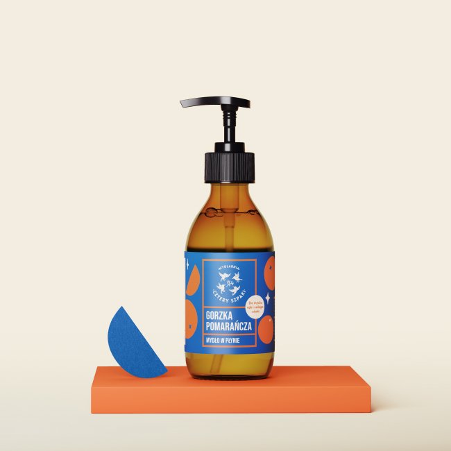 Brązowa butelka z pompką z niebieską etykietą z pomarańczową grafiką jest umieszczona na pomarańczowej platformie na beżowym tle. 