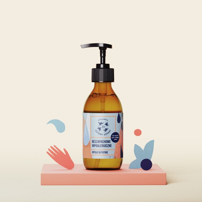 Na różowej platformie eksponowana jest brązowa butelka z pompką hipoalergicznego, bezzapachowego mydła w płynie. Etykieta zawiera niebieskie i pomarańczowe akcenty oraz zabawne abstrakcyjne kształty otaczające butelkę.